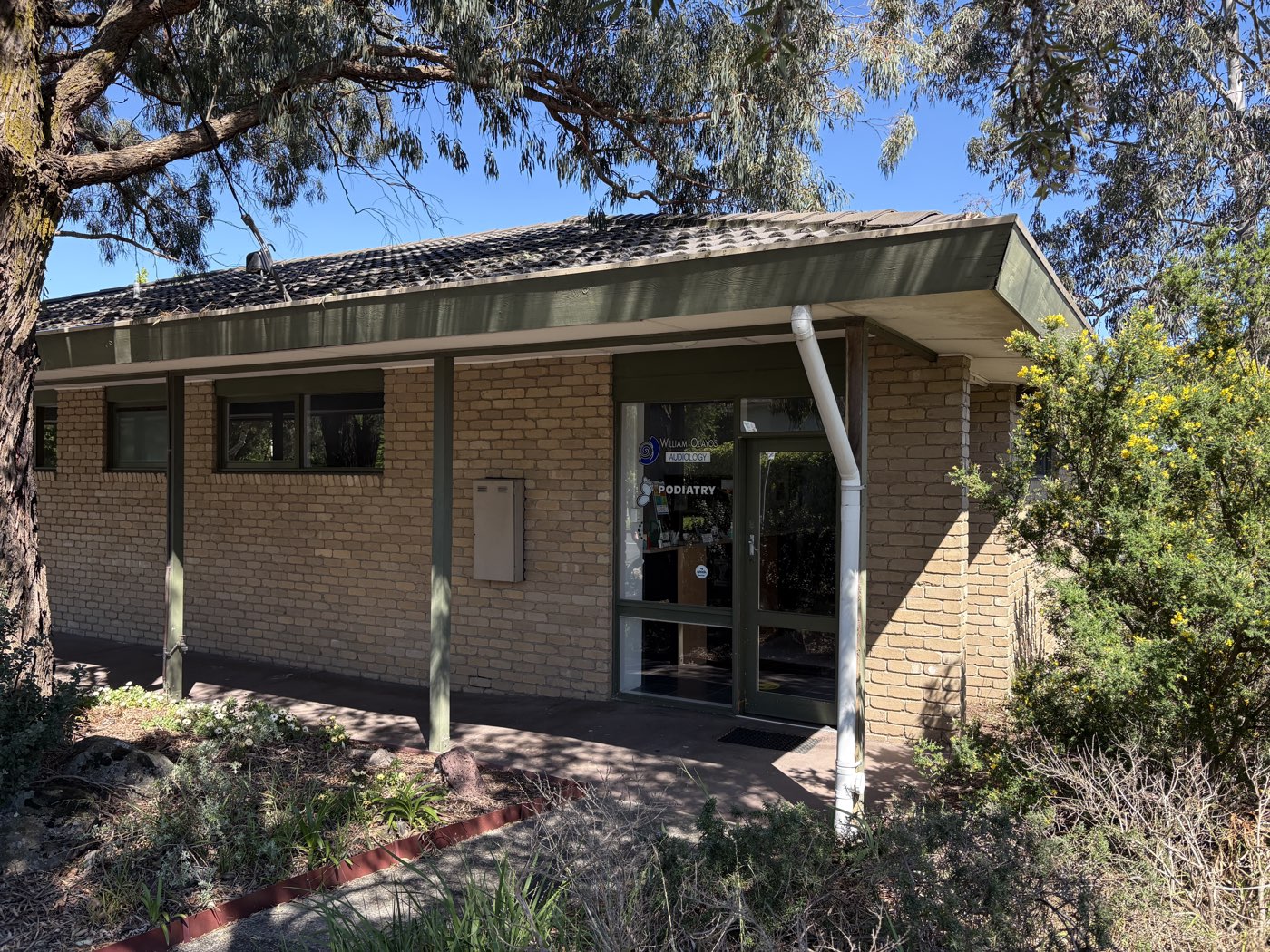 The entrance to the Precision Acoustics clinic at 1034 Doncaster Road, a brick building with a green awning and a glass front door